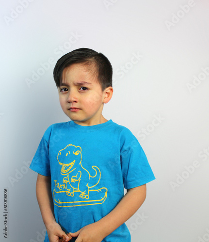 Sad and Angry kid, looking sideways, about to cry, 5 year-old boy, feelings, emotion, unhappy, latin boy, light skin, medium shot, black hair, white background,  body three-quarter view, blue t-shirt