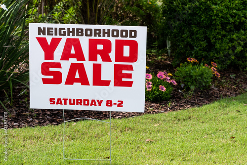 Neighborhood Yard Sale Sign placed in yard with flowers blurred in background