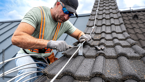Work on the roof. An electrician installing a lightning rod conductor on a tiles roof. photo