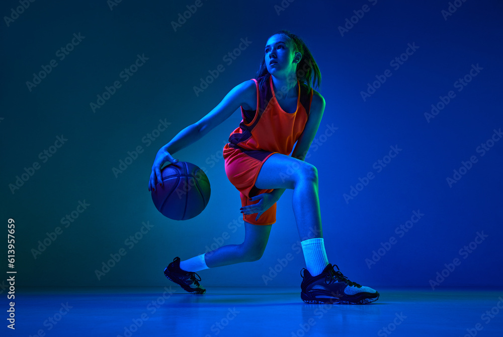 Motivation to win. Young female basketball player in motion during game against blue studio background in neon light. Concept of professional sport, action and motion, game, competition, hobby, ad