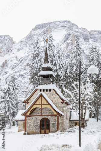 Beautiful view of Chapel by Braies Lake completely iced in a snowy winter day; Alto-Adige, Italy; Dolomites
