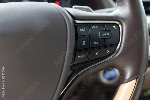 Cruise control, speed limit and volume buttons on modern car steering wheel, interior details. Hybrid car with adaptive cruise control radar. Buttons on the steering wheel © uflypro