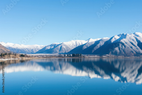 A majestic mountain range blanketed in fresh snow, with clear blue skies and a frozen lake in the foreground