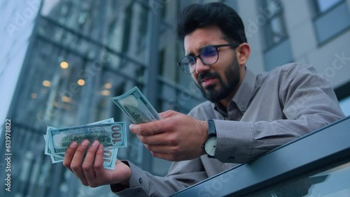 Upset Arabian Indian man cash owner businessman hold hundred dollars on city office terrace outdoors count lack money tight poor salary minimum wage business debt financial crisis throw banknotes away photo