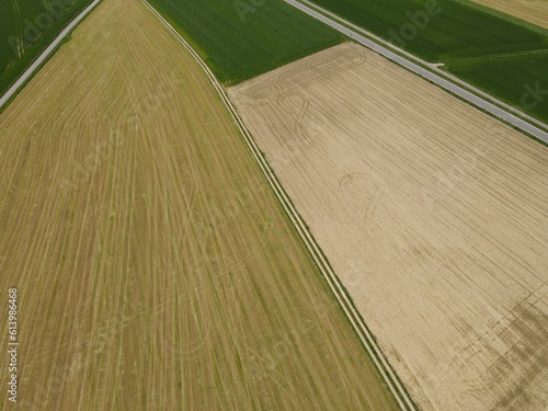Aerial view of plowed fields with soil, green growth crop fields, a long country road and a asphalt road in spring 