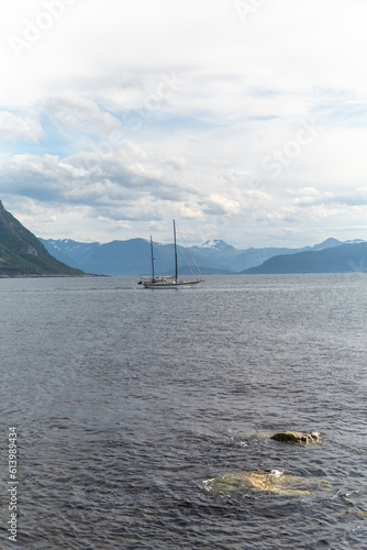 Boat sailing in open sea with big mountains, fjords in the background. Boat setting sail in with big mountains