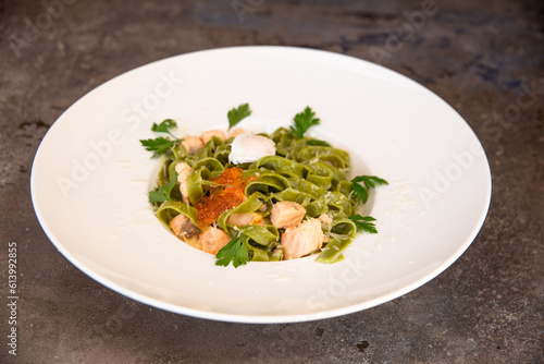 green pasta with salmon and red caviar and greens in a white plate