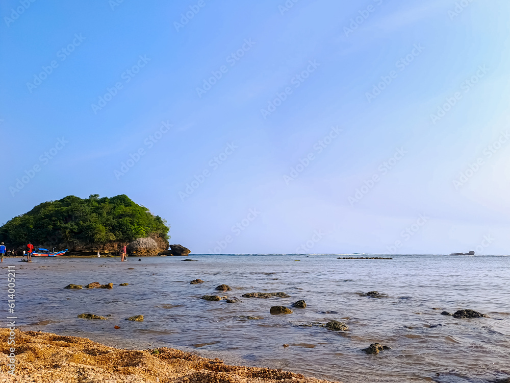Low tidewater in a beautiful beach with sand, rocks and green vegetation under clear blue sky during a summer vacation. Kondang Merak Beach, Malang, Indonesia