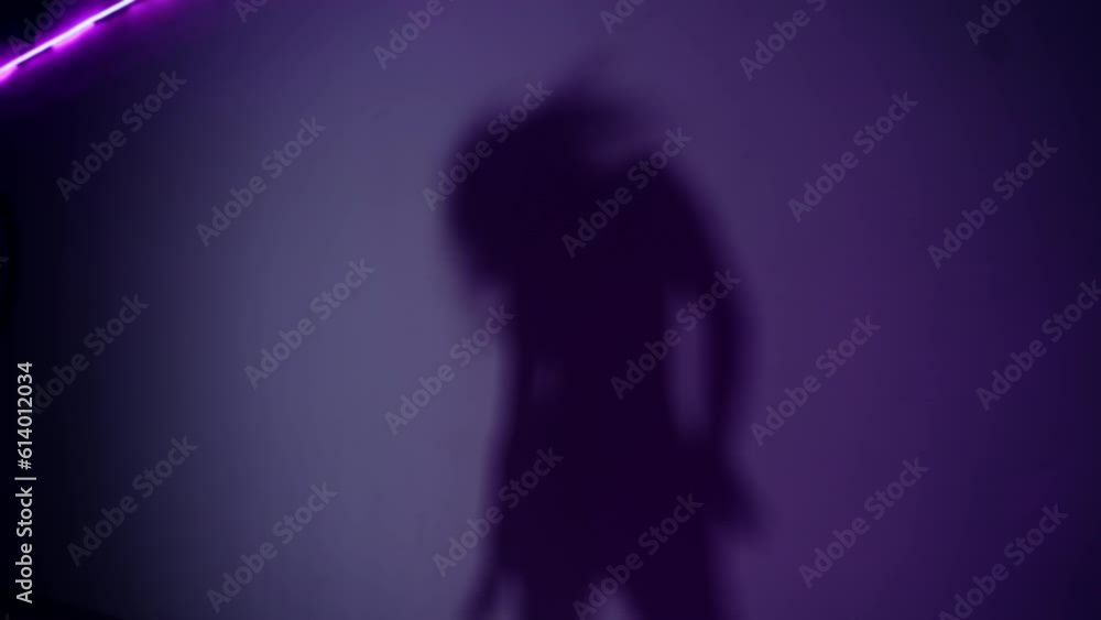 Female shadow moving gracefully on the purple wall. Woman dancing in the dark room. Female shadow moving gracefully on the purple wall. Woman dancing in the dark room.