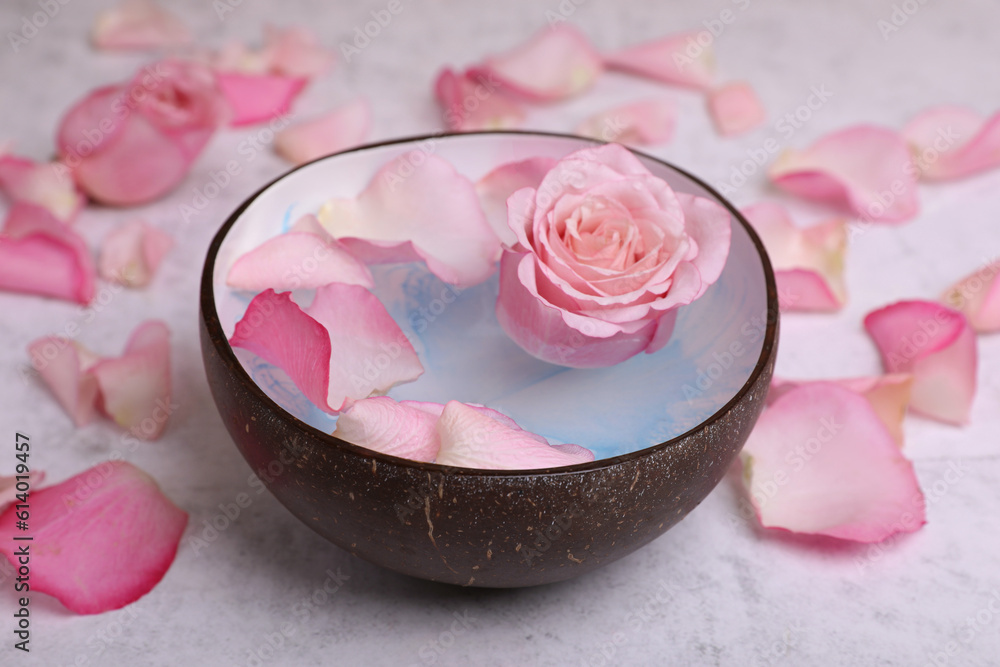 Beautiful composition with bowl of water and rose petals on light table, closeup. Spa treatment