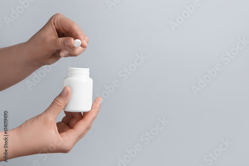 Woman holding pill and bottle on light grey background, closeup. Space for text