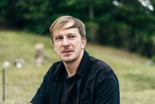 portrait of a young guy with blond hair in a black T-shirt in nature
