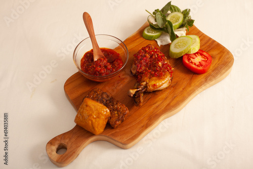 Ayam penyet (smashed fried chicken) is Indonesian East Javanese cuisine, served with tofu, tomato, sambal chili, lettuce and cucumber slice.