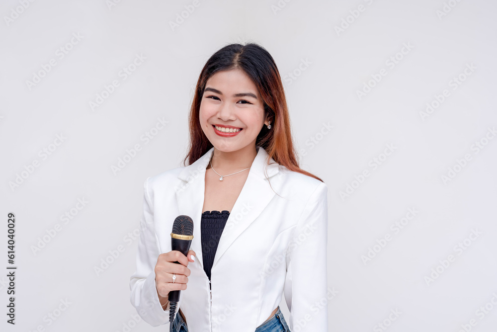 A cheerful young woman holding a microphone near her chest while smiling at the camera. Isolated on a white background. A cheerful young woman holding a microphone near her chest while smiling at the camera. Isolated on a white background.