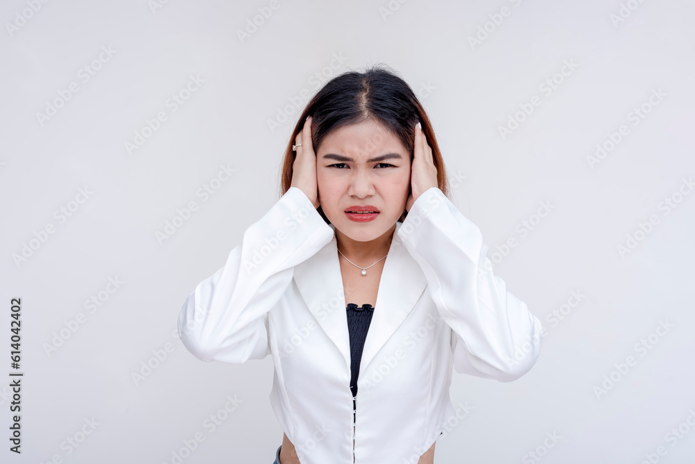 An overwhelmed young woman covering her ears in distress while looking at the camera. Isolated on a white background. An overwhelmed young woman covering her ears in distress while looking at the camera. Isolated on a white background.