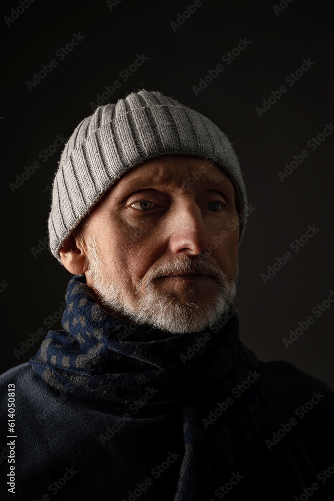 portrait of a sad adult man with a white beard and wearing a scarf and hat on a black background, close-up, selective focus