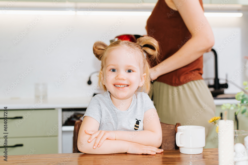 Portrait of cute happy girl in kitchen, caucasian smiling child sitting at table and looking at camera Portrait of cute happy girl in kitchen, caucasian smiling child sitting at table and looking at camera