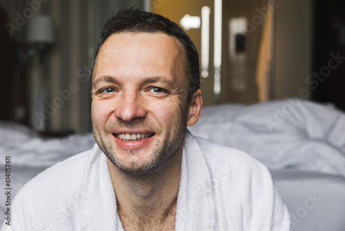 Portrait of smiling young adult European man in white bathrobe