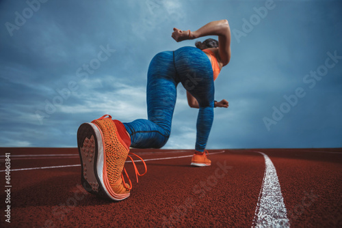 Close up wide angle view of a female sprinter athlete getting ready to start a race on a tartan racetrack