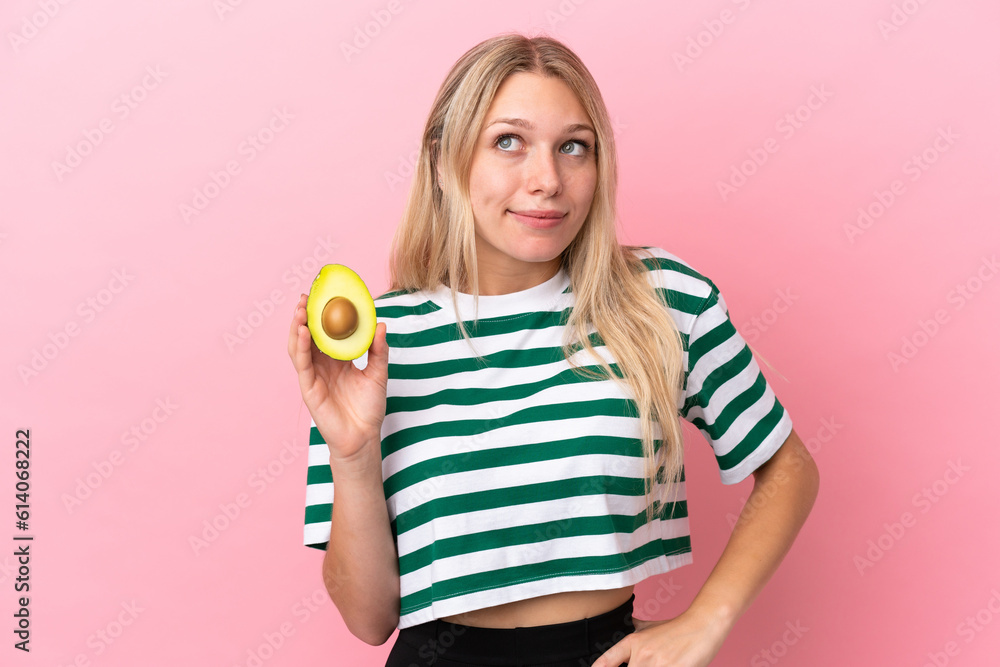 Young caucasian woman holding an avocado isolated on pink background having doubts and thinking Young caucasian woman holding an avocado isolated on pink background having doubts and thinking
