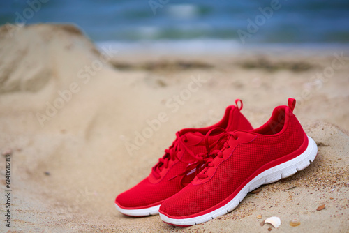 Red ladies shoes on empty sandy beach. 1 pair of sport and leisure shoes.