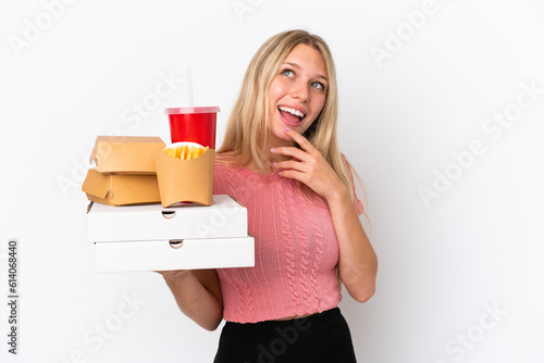 Young caucasian woman holding fat food isolated on blue background looking up while smiling