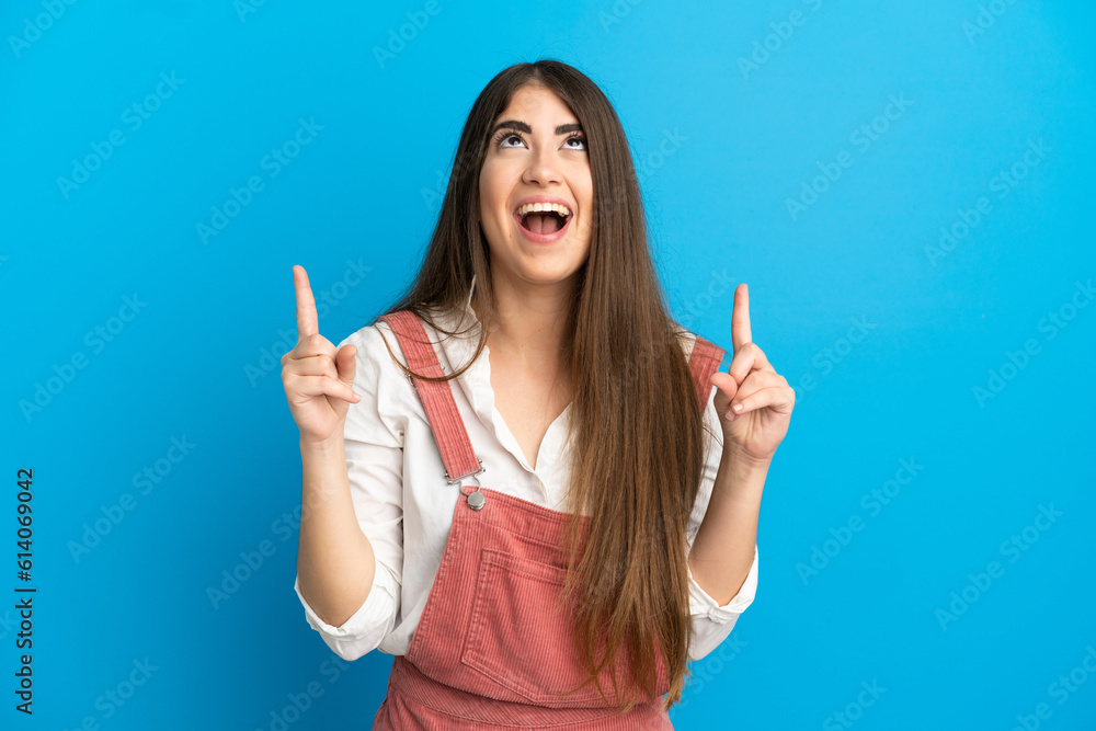 Young caucasian woman isolated on blue background surprised and pointing up Young caucasian woman isolated on blue background surprised and pointing up