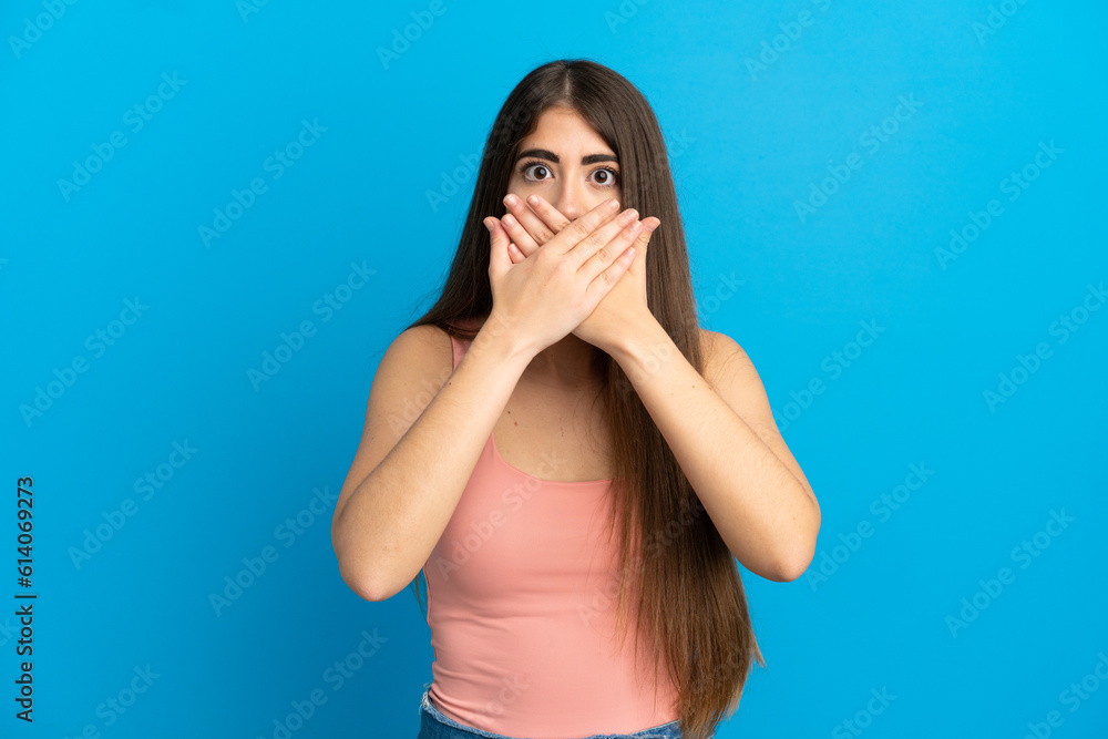 Young caucasian woman isolated on blue background covering mouth with hands Young caucasian woman isolated on blue background covering mouth with hands