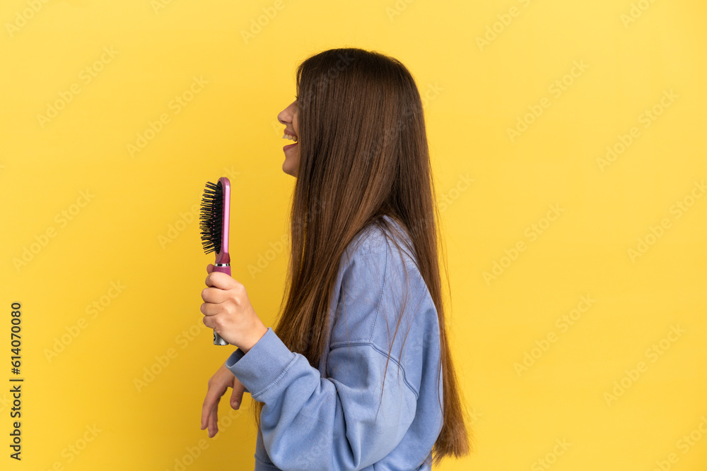 Young caucasian woman holding hairbrush isolated on blue background laughing in lateral position Young caucasian woman holding hairbrush isolated on blue background laughing in lateral position