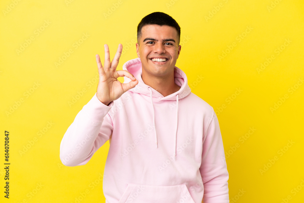 Young handsome man over isolated yellow background showing ok sign with fingers