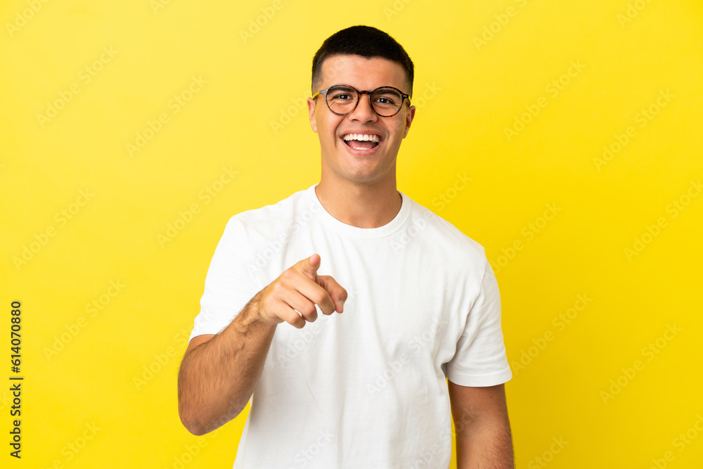 Young handsome man over isolated yellow background surprised and pointing front Young handsome man over isolated yellow background surprised and pointing front