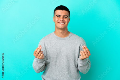 Young handsome man over isolated blue background making money gesture © luismolinero