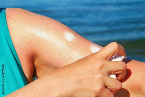 Middle-aged woman wearing in swimsuit applying sunblock cream lotion on sea beach in sunny day, closeup,