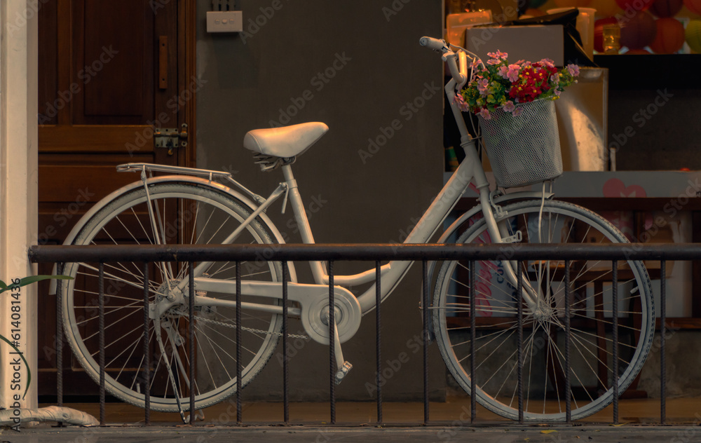 A white bicycle with a cart full of colorful flowers, in a corner of the cafe with warm vintage yellow. Decorative bicycle concept. Vintage photo.