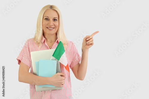Mature woman with flag of Italy  books and laptop pointing at something on white background