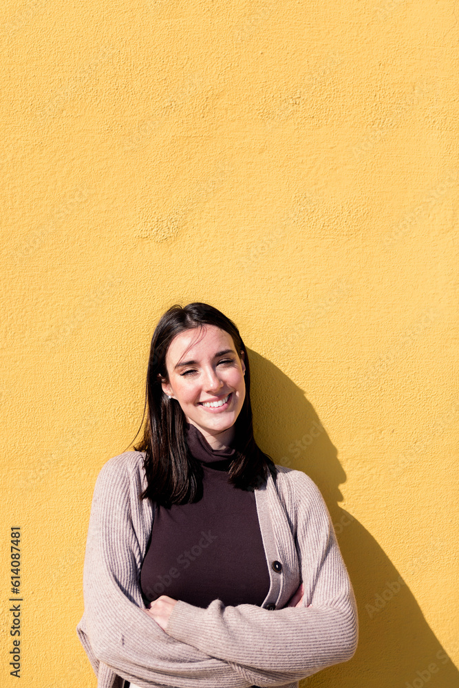 young woman smiling happy looking at camera with arms crossed leaning in a yellow background, concept of youth and lifestyle, copy space for text young woman smiling happy looking at camera with arms crossed leaning in a yellow background, concept of youth and lifestyle, copy space for text