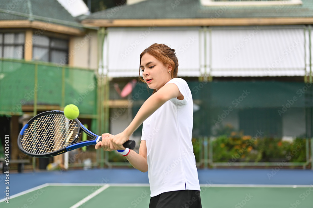 Shot of young female athlete hitting tennis ball flying towards her. Sport, training, competition and active life concept