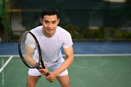 Focused male tennis player crouching in ready position and holding racket while waiting for serving ball from competitor