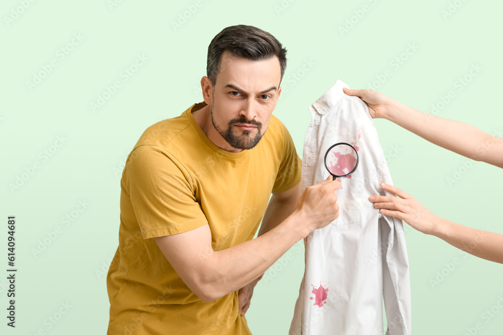 Handsome man with magnifier examining stained shirt on green background Handsome man with magnifier examining stained shirt on green background