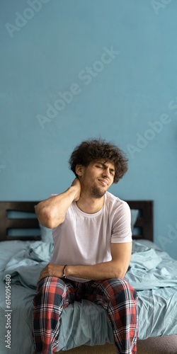 Pain in the neck. Attractive man sitting on the bed and holding a painful neck. People with body-muscles problem. Healthcare And Medicine concept.