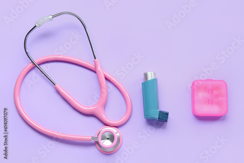 Composition with asthma inhaler, stethoscope and box of pills on lilac background