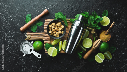 Mojito. Shaker, sugar, fresh lime and mint on wooden board. On a black stone background. Top view.