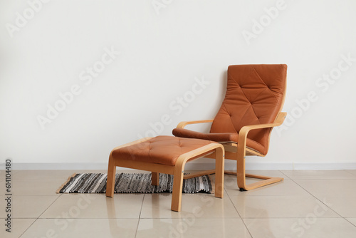 Cozy brown armchair with foot stool and stylish rug near white wall