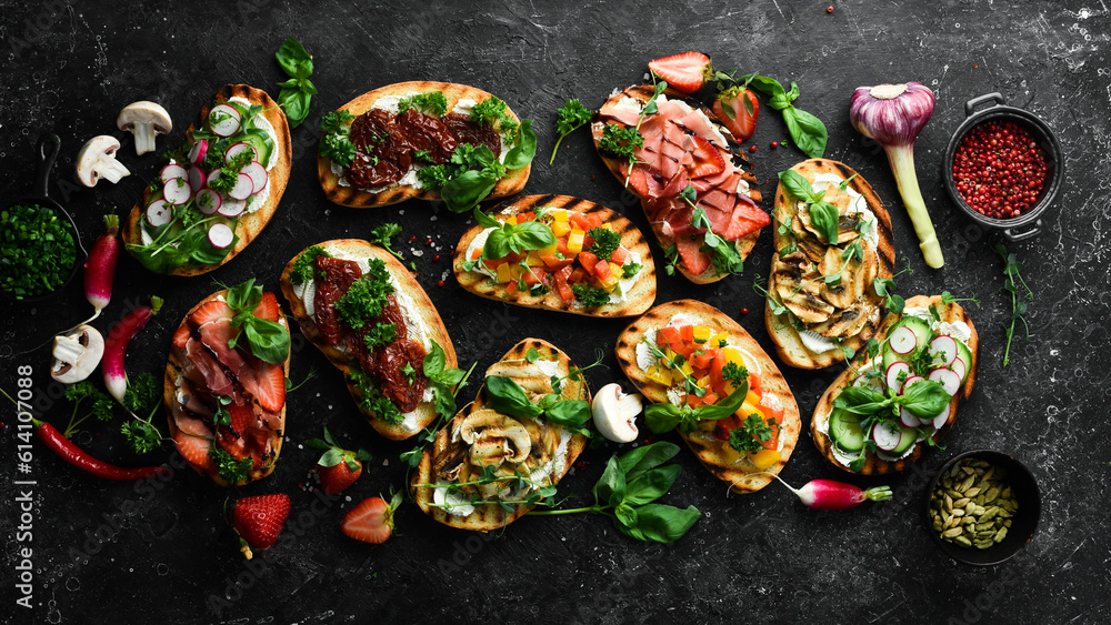 Set of colored sandwiches with tomatoes, prosciutto, vegetables and cheese on a black stone background. Bruschetta. Top view.