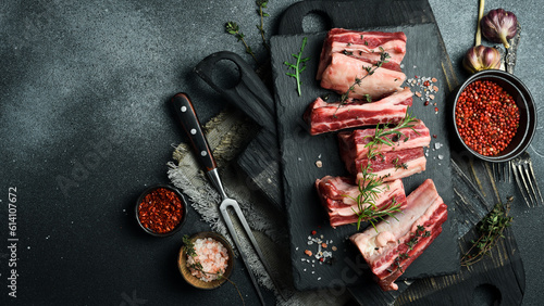 Fresh raw veal ribs with rosemary, spices and herbs. On a dark slate background. Top view. Free space for text.