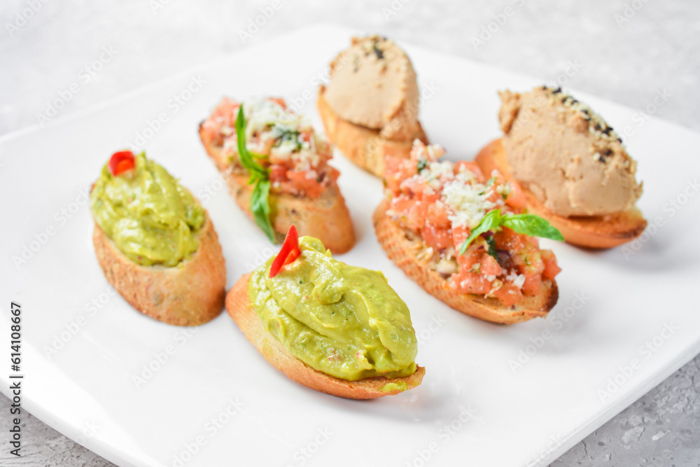 Set bruschetta. Sandwiches with avocado, liver pâté and vegetables. On a white plate. On a gray stone background. Restaurant menu.