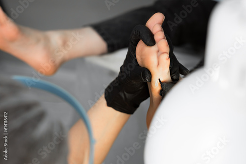 A close-up of the process of making a pedicure by a master. Treatment of the skin of the foot with tools. Removal of an old callus with a scalpel.  photo