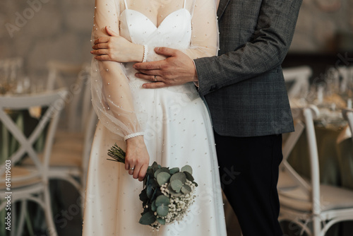 Obraz na płótnie Groom hugs bride waist. Bride holding wedding bouquet. Close-up. Rings on the fingers. w salonie