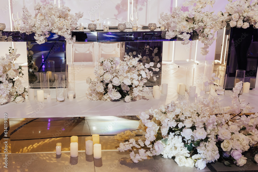 Luxury elegant classic table for the bride and groom decorated with white flowers and vases with candles.