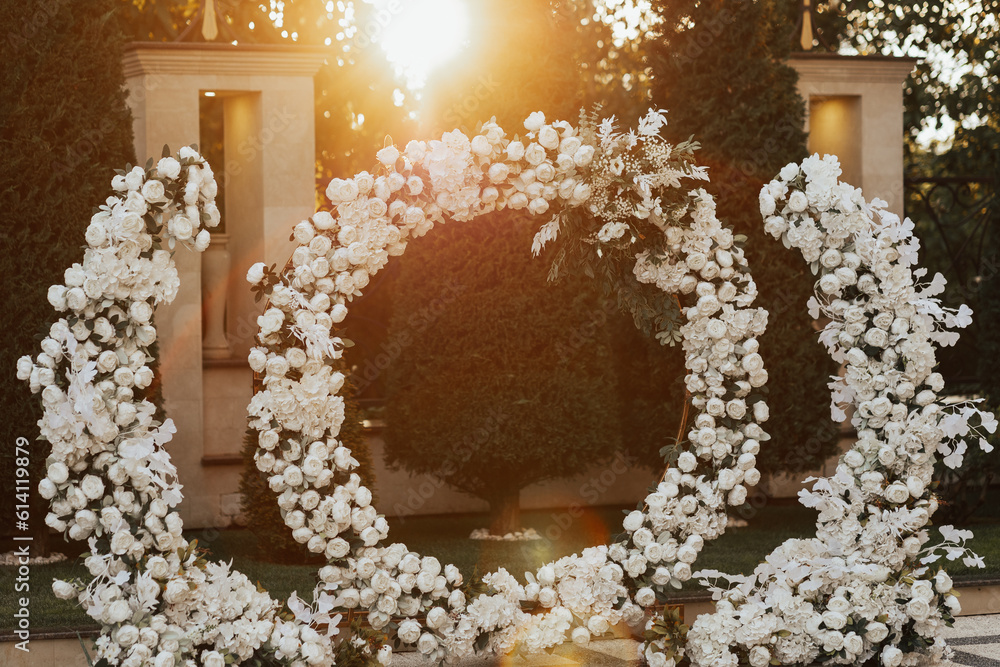 Wedding ceremony in the garden at the sunset. Beautiful wedding round arch decorated with white flowers and greenery outdoors